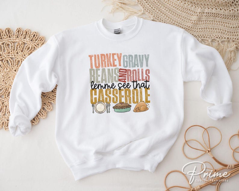 May include: White sweatshirt with a Thanksgiving themed graphic that says "Turkey Gravy Beans and Rolls lemme see that Casserole". The graphic features a turkey, a casserole dish, and a roll.