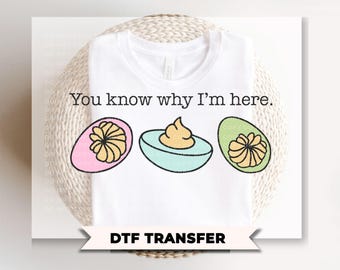 May include: White t-shirt with the text "You know why I'm here." and a graphic of three deviled eggs. The eggs are pink, blue, and green, with yellow filling. The bottom of the image reads "DTF TRANSFER".