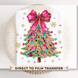 May include: White t-shirt featuring a colorful Christmas tree design with a large pink bow at the top. The tree is decorated with gold glitter, colorful ornaments, and snowflakes. The text "DIRECT TO FILM TRANSFER" is at the bottom.