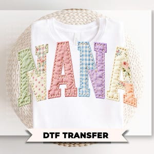 May include: White t-shirt with the word "NANA" in colorful, patchwork-style letters. The letters are in shades of green, pink, blue, and purple, with floral and gingham patterns. The text "DTF TRANSFER" is below the shirt.