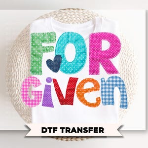 May include: White t-shirt with the word "FORGIVEN" in colorful, patchwork-style letters. The letters are in various patterns and colors, including green polka dots, teal, pink, orange, purple, and blue gingham. A small navy blue heart is between the "FOR" letters. The text "DTF TRANSFER" is below.