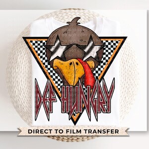 May include: A white t-shirt with a graphic of a turkey wearing sunglasses and a checkered background. The text "Def Hungry" is in red and black lettering. The shirt is for direct to film transfer.