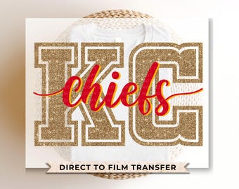May include: Gold glitter letters spelling "KC Chiefs" in a red and yellow font on a white t-shirt.  Direct to film transfer.