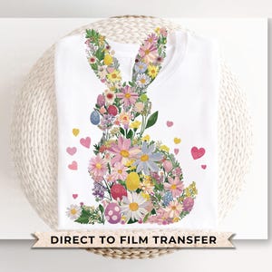 Op de afbeelding: Een wit T-shirt met een bloemenontwerp van een konijn. Het ontwerp is gemaakt van roze, paarse en witte bloemen. De tekst "Direct to Film Transfer" staat onderaan het shirt gedrukt.