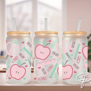 May include: Three frosted glass tumblers with bamboo lids and clear straws. Each tumbler features a pink and green pattern of apples, hearts, pencils, scissors, and paper clips.