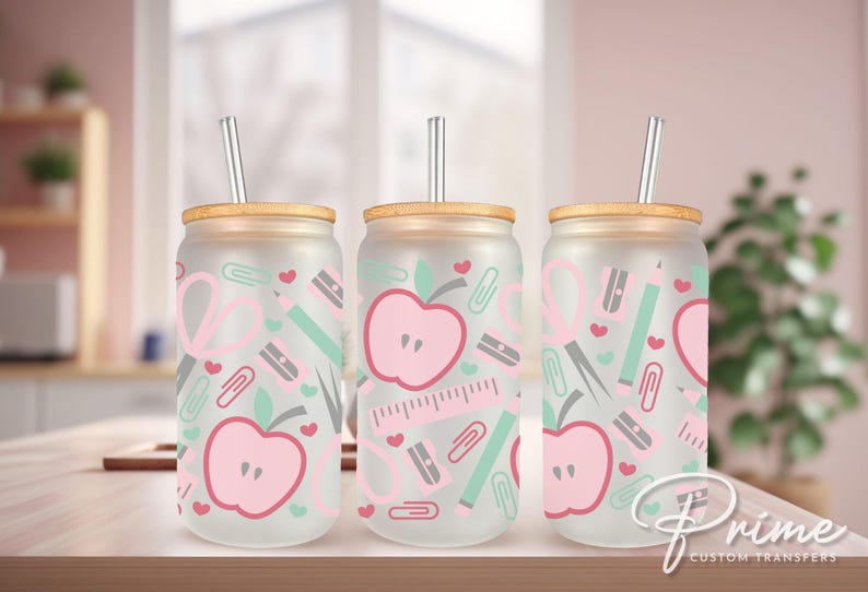May include: Three frosted glass tumblers with bamboo lids and clear straws. Each tumbler features a pink and green pattern of apples, hearts, pencils, scissors, and paper clips.
