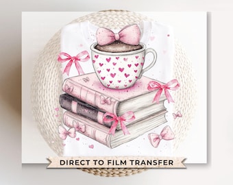 Könnte beinhalten: Eine rosa-weiße Kaffeetasse mit Herzmuster steht auf einem Stapel Bücher mit rosa Schleifen. Der Text "Direct to Film Transfer" befindet sich am unteren Rand des Bildes.