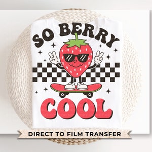 May include: White t-shirt with a red strawberry wearing sunglasses and skateboarding. The text "So Berry Cool" is printed on the shirt in a retro font.