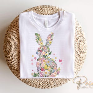 Op de afbeelding: Wit T-shirt met een bloemig konijnontwerp. Het konijn is gemaakt van roze, paarse en gele bloemen. Er zijn kleine roze hartjes rond het konijn verspreid.