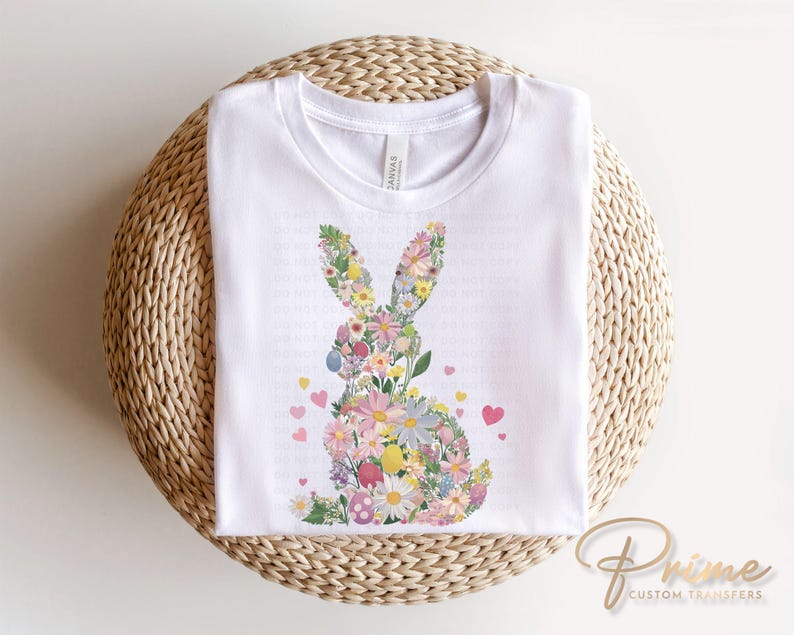 Op de afbeelding: Wit T-shirt met een bloemig konijnontwerp. Het konijn is gemaakt van roze, paarse en gele bloemen. Er zijn kleine roze hartjes rond het konijn verspreid.