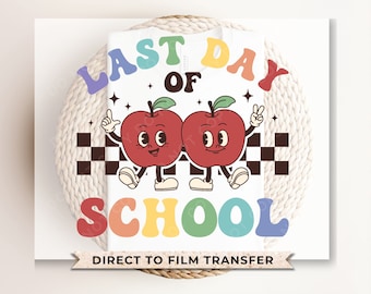 May include: A white t-shirt featuring a graphic with the text LAST DAY OF SCHOOL in colorful, wavy letters. The design includes two red cartoon apples with faces, arms, and legs, positioned above a black and white checkered pattern.