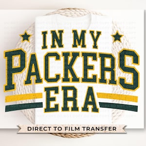 May include: A white t-shirt with a green and yellow graphic that says "In My Packers Era". The graphic has a vintage style and is perfect for a fan of the Green Bay Packers.