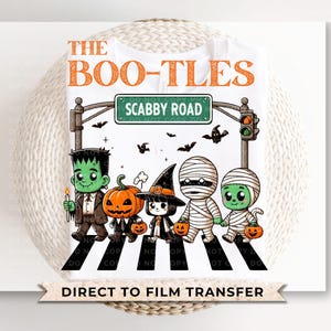 May include: A white t-shirt with a graphic of a crosswalk with four cartoon characters dressed as monsters and pumpkins. The text "THE BOO-TLES" and "SCABBY ROAD" are on the shirt. The text "DIRECT TO FILM TRANSFER" is at the bottom of the shirt.