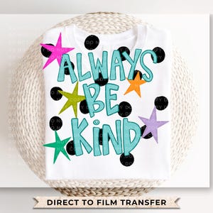 May include: White t-shirt featuring the phrase "ALWAYS BE KIND" in turquoise, with black outlines. The design includes colorful stars and black polka dots. The words "DIRECT TO FILM TRANSFER" are at the bottom.
