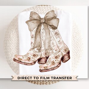 May include: A pair of brown and white cowboy boots with floral designs. The boots are tied together with a brown ribbon bow. The image includes the text "DIRECT TO FILM TRANSFER".