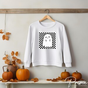 May include: White sweatshirt with a black and white checkered square design featuring a cartoon ghost with a smiling face.