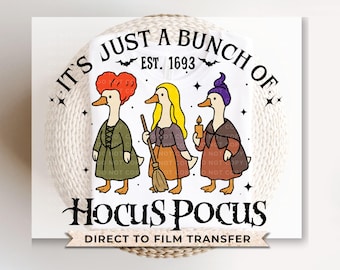May include: White t-shirt featuring a graphic of three duck characters dressed as witches, with the text "IT'S JUST A BUNCH OF" above and "Hocus Pocus" below. The design includes the text "EST. 1693" and a bat symbol.