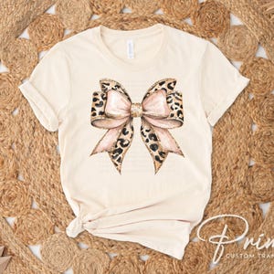 May include: A beige t-shirt with a large pink and brown leopard print bow design.