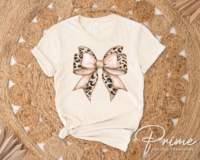 May include: A beige t-shirt with a large pink and brown leopard print bow design.