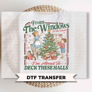 May include: A white t-shirt featuring a vintage-style graphic of two children decorating a Christmas tree with a small dog nearby. The text reads From The Windows To The Walls I'm About To DECK THESE HALLS in green and red lettering.