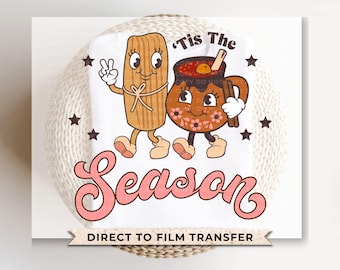 Op de afbeelding: Een wit strijktransferontwerp met een cartoon tamale en een cartoon mok met warme chocolademelk met de tekst "'Tis The Season".