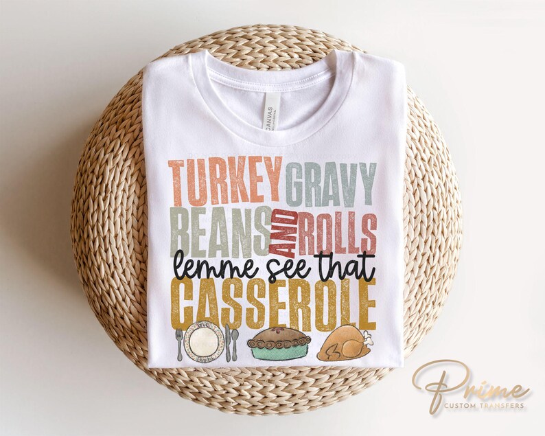May include: White t-shirt with a Thanksgiving themed graphic that says "Turkey Gravy Beans and Rolls lemme see that Casserole".