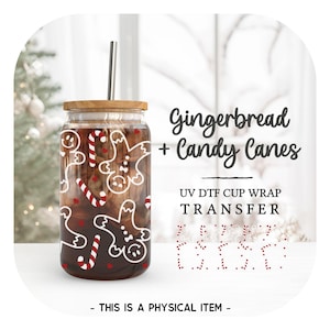 May include: A clear glass cup with a wooden lid and a metal straw. The cup is decorated with a red and white gingerbread man and candy cane design. The text "Gingerbread + Candy Canes" and "UV DTF Cup Wrap Transfer" is printed on the image.