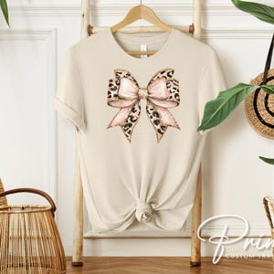 May include: A beige t-shirt with a large pink and brown leopard print bow on the front.