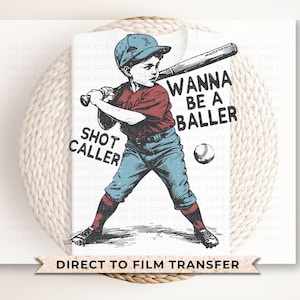 May include: A baseball-themed graphic featuring a young batter in a red shirt, blue pants, and a blue cap, holding a bat. The text "WANNA BE A BALLER" and "SHOT CALLER" are displayed. A baseball is also visible. The image is a direct to film transfer.
