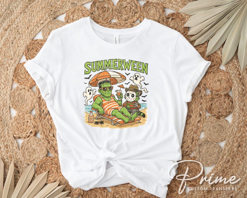 May include: White t-shirt with a colorful graphic that reads "Summerween." The graphic features Frankenstein and Freddy Krueger relaxing on a beach, under an umbrella. The design includes ghosts, a beach scene, and a cocktail.