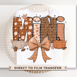 May include: White t-shirt with the word "MINI" in a fall-themed design. The letters are decorated with polka dots, floral patterns, and leopard print. Pumpkins and a bow accent the design. The text "DIRECT TO FILM TRANSFER" is at the bottom.
