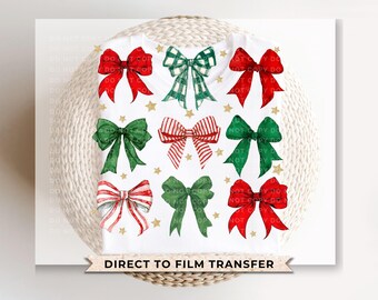 May include: White t-shirt with nine watercolour bows in red, green, and white, with gold star accents. The bows have various patterns, including stripes and plaid. The text "DIRECT TO FILM TRANSFER" is at the bottom.