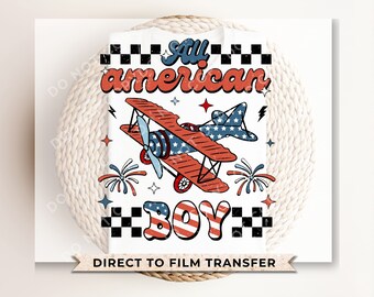 May include: A white t-shirt with a red, white, and blue airplane design. The text "All American Boy" is in a retro font with a checkered border. The words "Direct to Film Transfer" are printed at the bottom of the shirt.