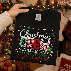 Op de afbeelding: Een zwart T-shirt met ronde hals en de tekst Christmas CREW in een mix van groene, rode en witte zuurstokpatronen. Daaronder staat de tekst A LITTLE BIT CRAZY, A LITTLE BIT LOUD, A WHOLE LOTTA LOVE, versierd met sneeuwvlokken en zuurstokken.