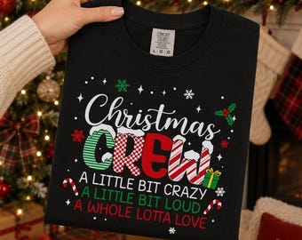 May include: A black crewneck t-shirt featuring the text Christmas CREW in a mix of green, red, and white candy cane patterns. Below, the text reads A LITTLE BIT CRAZY, A LITTLE BIT LOUD, A WHOLE LOTTA LOVE, accented with snowflakes and candy canes.