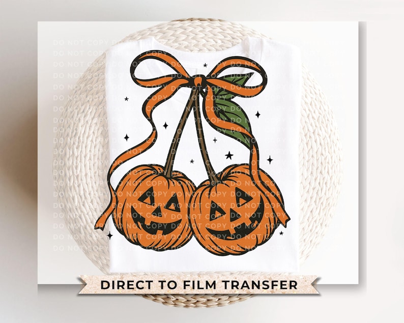 May include: White t-shirt featuring a Halloween-themed design. The design includes two orange pumpkin faces with black cut-out eyes and mouths, connected by brown stems and adorned with orange ribbons and green leaves. The text "DIRECT TO FILM TRANSFER" is at the bottom.