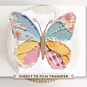 May include: White t-shirt featuring a large butterfly design. The butterfly wings are made of patchwork fabric in various colors and patterns, including floral, gingham, and solid colors. The text "DIRECT TO FILM TRANSFER" is displayed below the shirt.