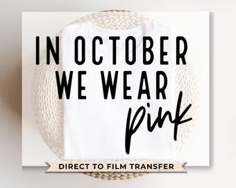 May include: White t-shirt with black text that reads "In October We Wear Pink" and the words "pink" are in a pink cursive font. The t-shirt is on a woven basket. The text "Direct to Film Transfer" is at the bottom of the image.