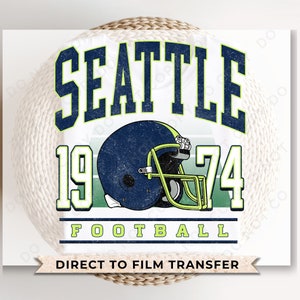May include: A white background with a green, white, and blue graphic design. The graphic features the text "Seattle 1974 Football" with a football helmet in the center. The text "Direct to Film Transfer" is at the bottom of the graphic.