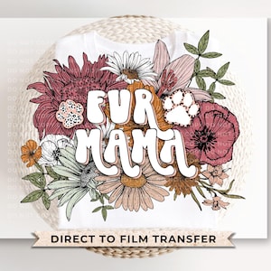 May include: White t-shirt featuring the text "FUR MAMA" in a retro font, surrounded by a floral design with pink, orange, and green flowers. A paw print is incorporated into the design. The words "DIRECT TO FILM TRANSFER" are at the bottom.