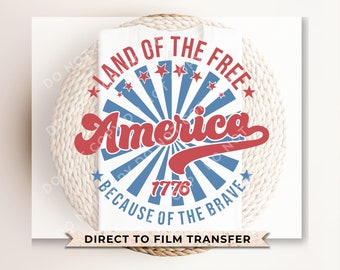 May include: A white t-shirt featuring a red, white and blue graphic design that reads "Land of the Free, America, Because of the Brave, 1776". The graphic is a circle with a red, white and blue starburst design. The text is in a retro font. The shirt is a direct to film transfer.