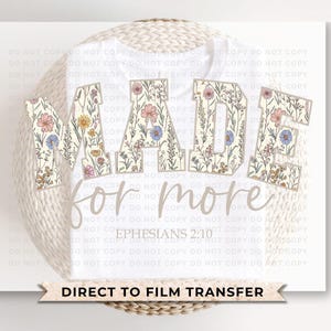 Puede incluir: Camiseta blanca con las palabras "MADE for more" en un dise&ntilde;o floral. El texto "Ephesians 2:10" est&aacute; debajo del texto principal. Las palabras "DIRECT TO FILM TRANSFER" est&aacute;n en la parte inferior.
