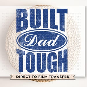 May include: A blue and white graphic design with the words "BUILT Dad TOUGH" in a distressed font. The word "Dad" is inside an oval shape. The phrase "DIRECT TO FILM TRANSFER" is at the bottom.