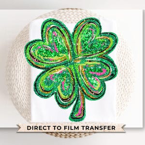 May include: A green four-leaf clover with glitter and gold accents on a white background. The text "Direct to Film Transfer" is below the clover.