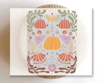 May include: A light gray t-shirt featuring a central orange pumpkin surrounded by a symmetrical graphic design. The print includes smaller orange pumpkins, pink and orange flowers, green leafy vines, a yellow crescent moon, and small stars.