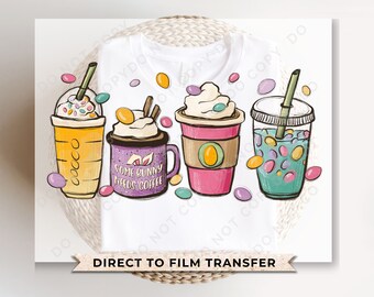 May include: A white t-shirt with a design of three colorful drinks with whipped cream and sprinkles. The drinks are surrounded by pastel-colored Easter eggs. The text "Some Bunny Needs Coffee" is on one of the drinks.