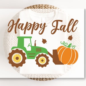 May include: A white t-shirt featuring the brown text Happy Fall above a green tractor graphic. The tractor has brown wheels with yellow sunflower centers and a brown front loader bucket carrying a large orange pumpkin with green vines.