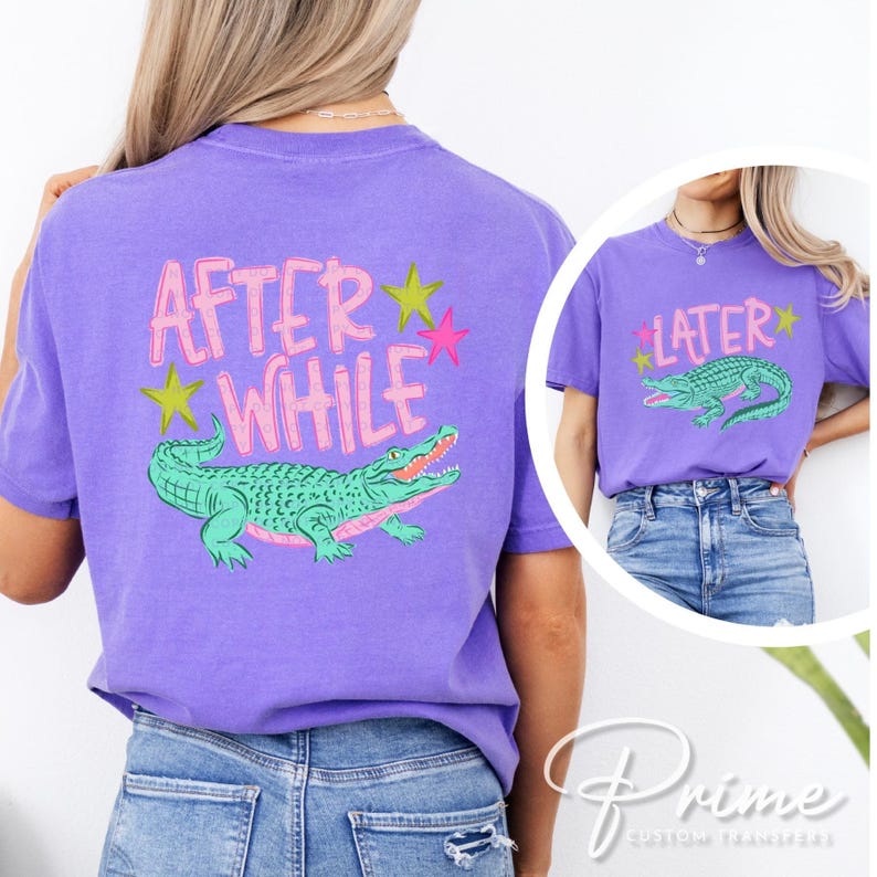 May include: A purple t-shirt with the text "AFTER WHILE" and a green alligator graphic on the back. The front of the shirt has the text "LATER" and a matching alligator graphic. The design includes pink and yellow stars.