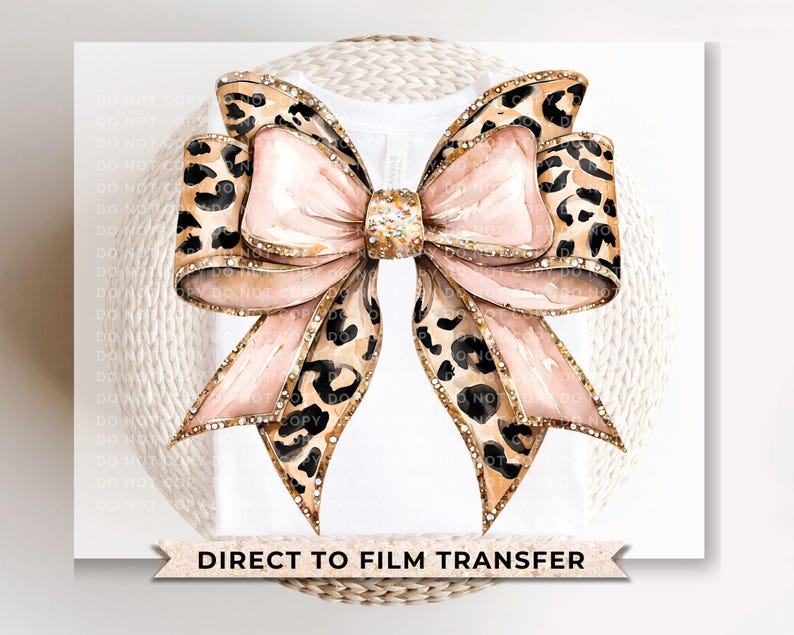 May include: A large pink bow with a leopard print pattern and gold accents. The bow is on a white background with the text "DIRECT TO FILM TRANSFER".