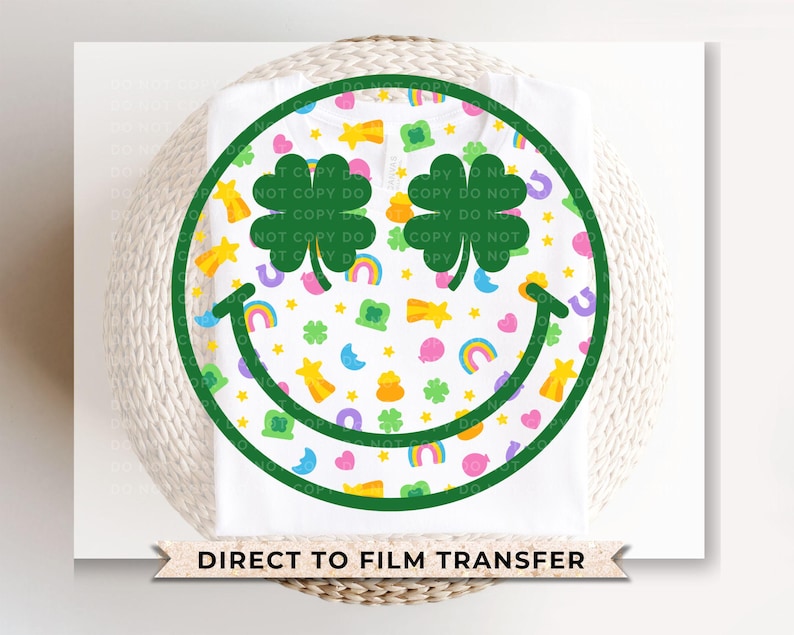 May include: White t-shirt featuring a green smiley face design with shamrocks, rainbows, and stars. The smiley face is outlined in green and filled with colorful St. Patrick's Day themed graphics. The text "DIRECT TO FILM TRANSFER" is at the bottom.